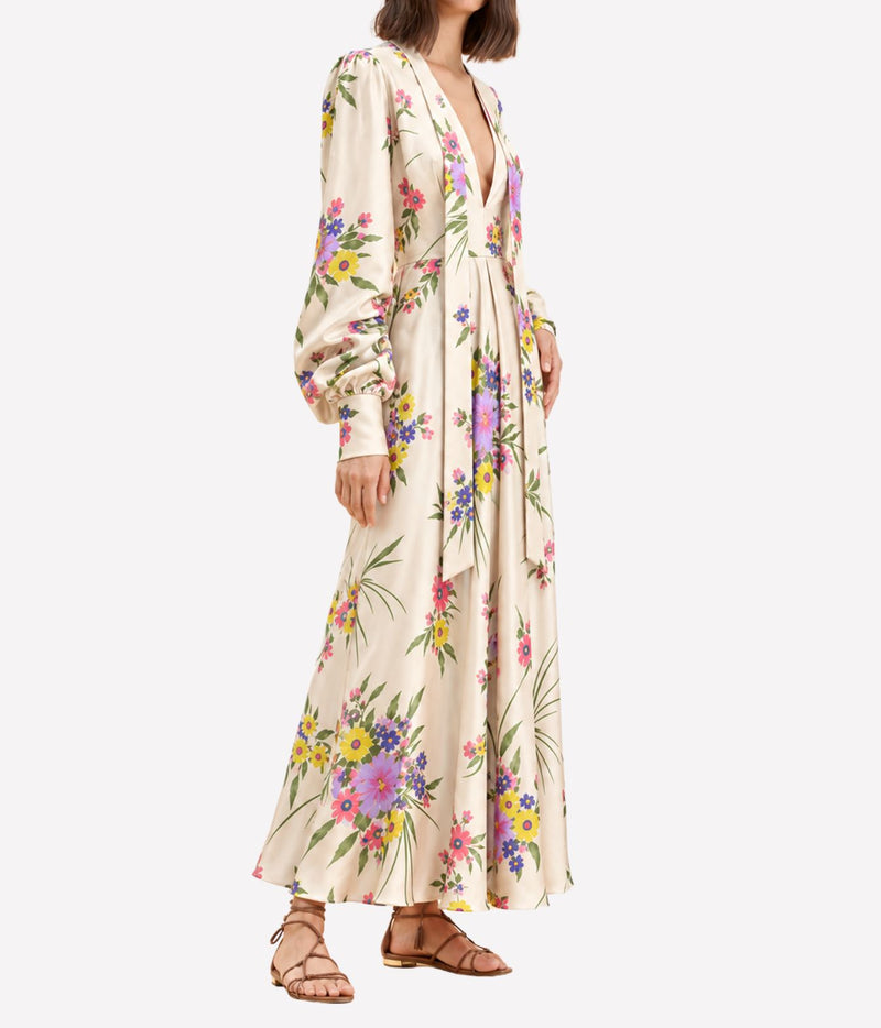 Side view of a model wearing the Raquel Diniz Valerie Dress in Pink Floral with tan strappy sandals, showing the fluid flared skirt and long sleeves