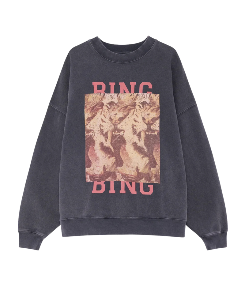 A dark gray washed crewneck sweatshirt featuring a large front graphic print with the word 'RING' in pink at the top and bottom, and a central square image of three lions in warm beige and brown tones.