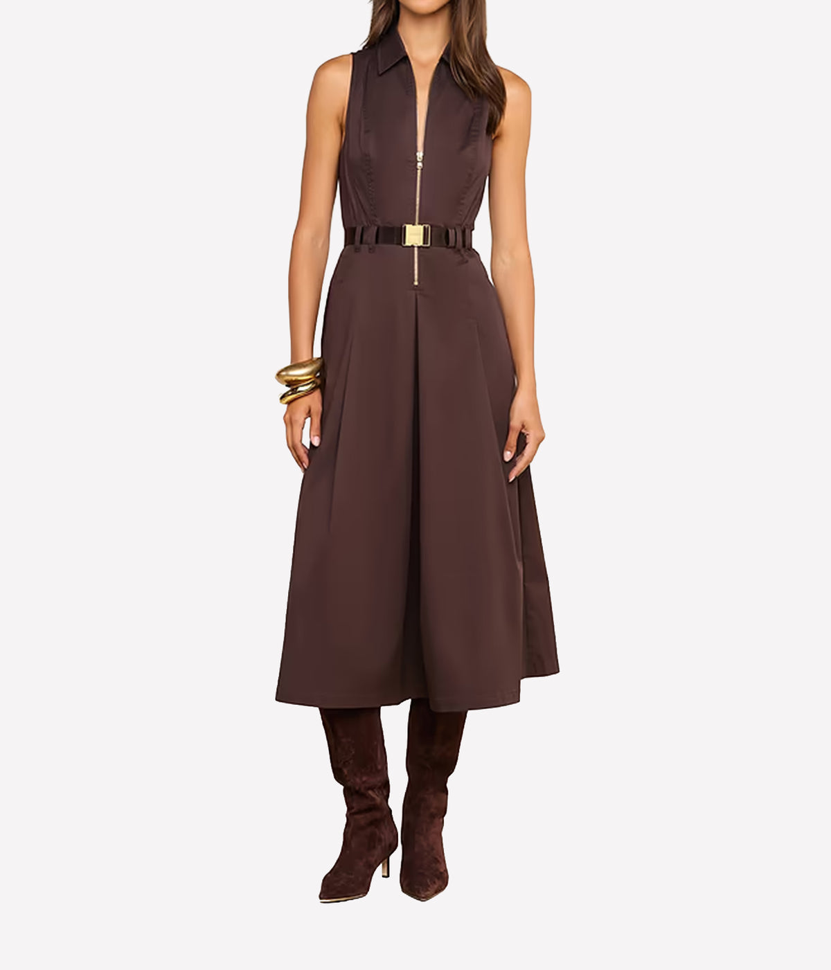 A woman models a sleeveless brown midi dress with a front zipper, a matching belt with a gold buckle, brown suede boots, and gold bracelets against a plain white background.