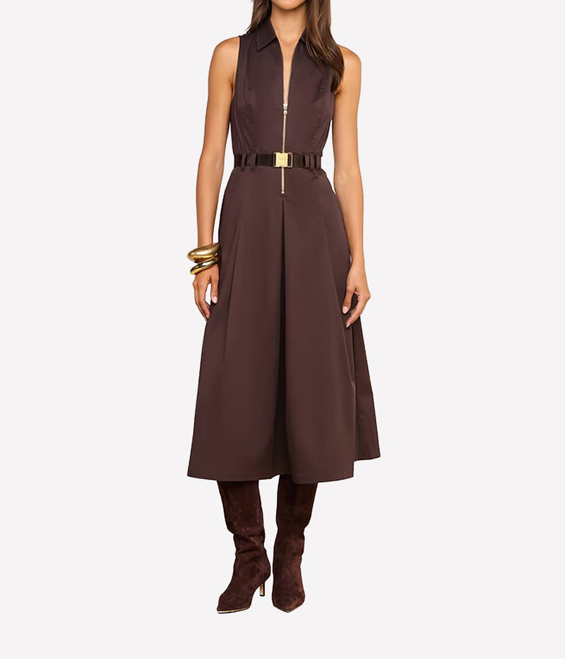 A woman models a sleeveless brown midi dress with a front zipper, a matching belt with a gold buckle, brown suede boots, and gold bracelets against a plain white background.