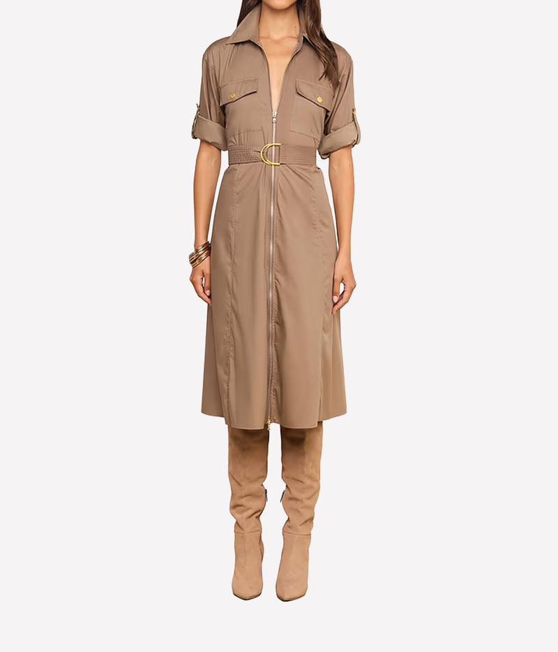 A model wearing a taupe-brown short-sleeve shirt dress with a front zipper, belt, and gold buckle, paired with matching taupe boots, against a light grey background.