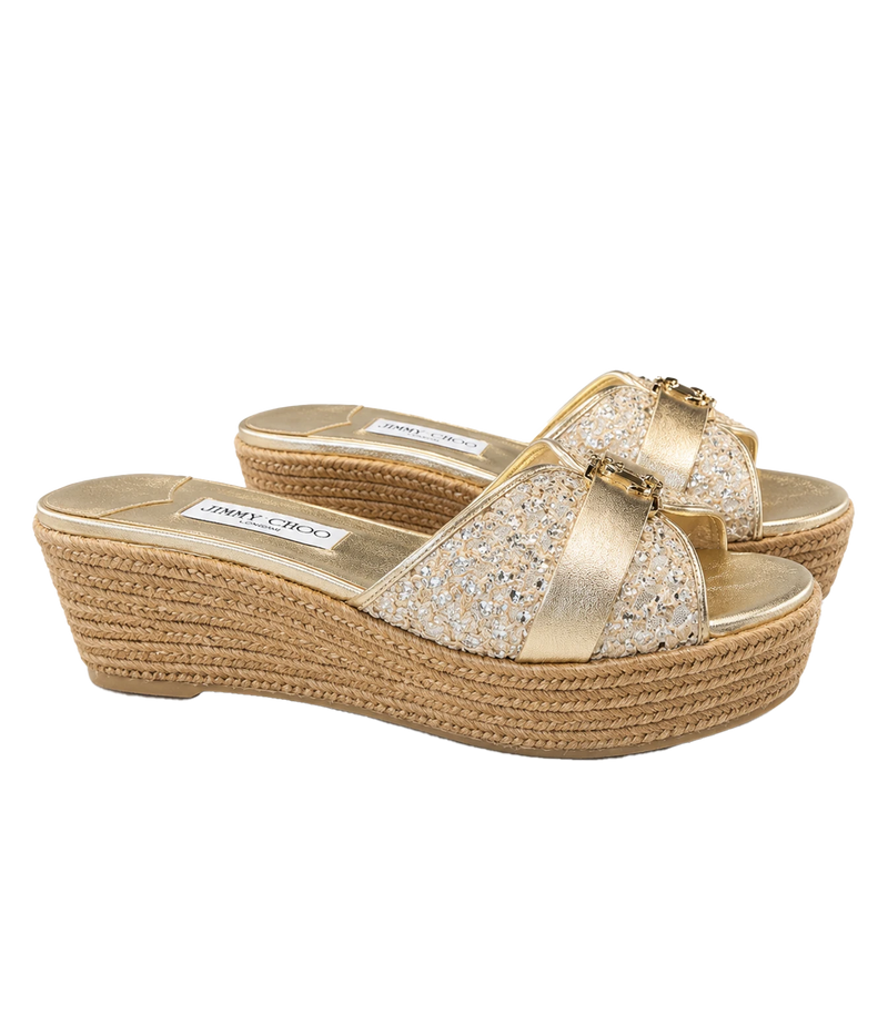 A pair of gold wedge espadrille sandals with glittery straps and a woven jute platform sole, shown on a plain white background.