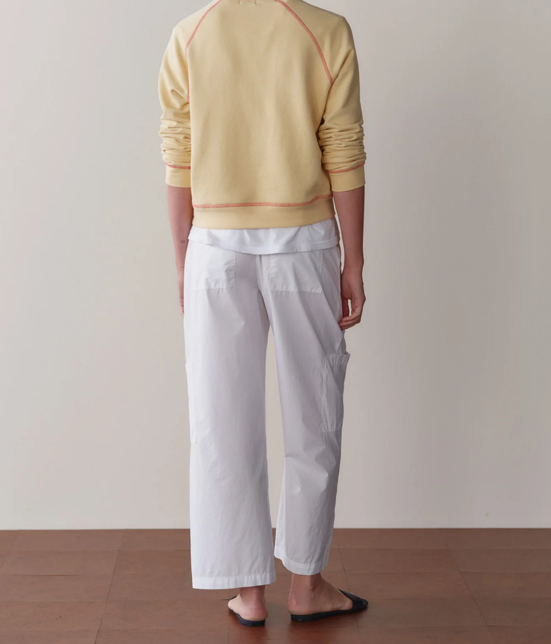 Back view of a model wearing the DONNI. The Pop Drawstring Cargo Pant in Powder, showing the back patch pockets and side cargo pocket, with a pale yellow sweatshirt and navy slides