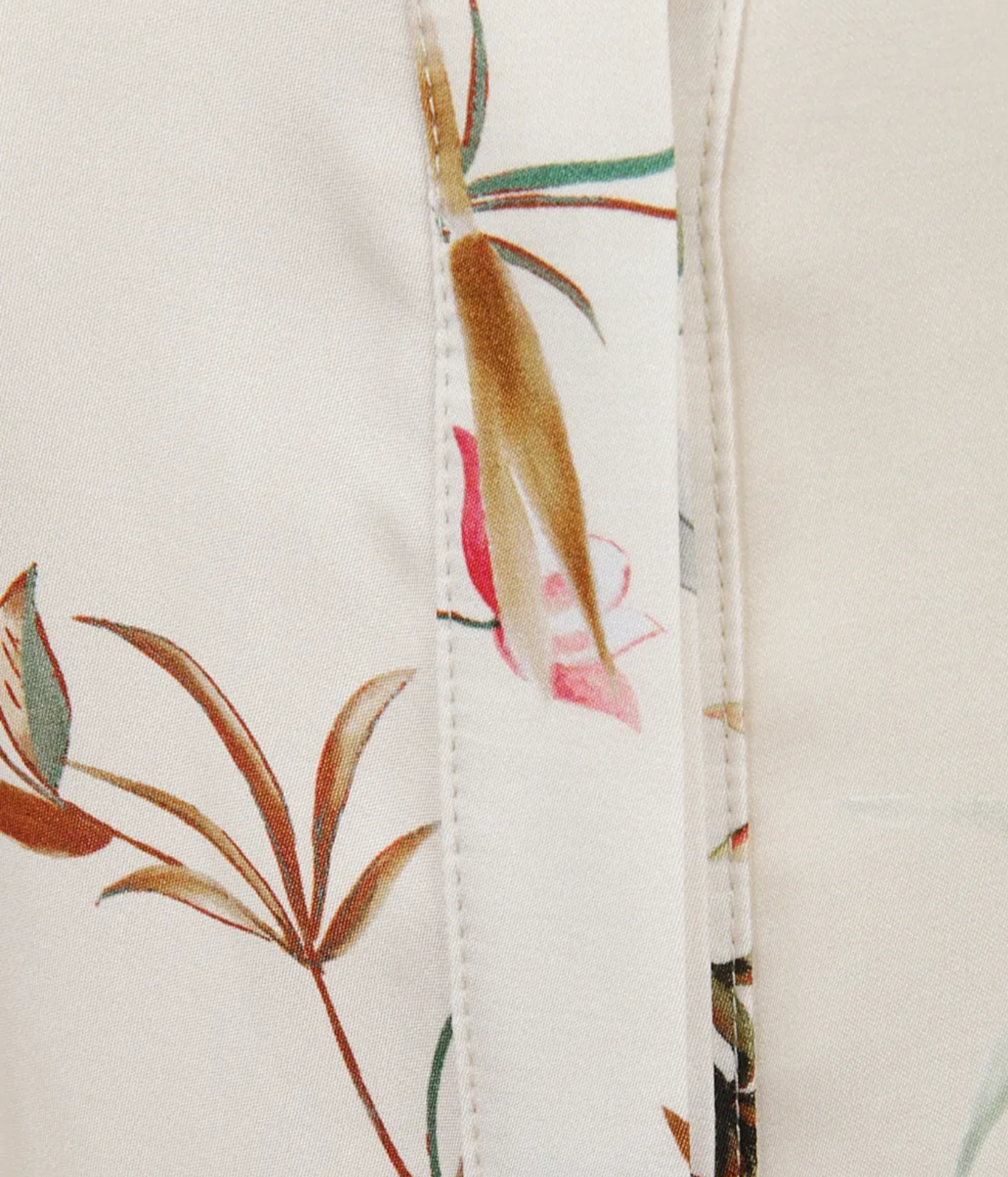 Close-up of a white fabric garment featuring a delicate botanical print with green leaves, brown bamboo stalks, and pink flower accents, detailed with a central vertical seam.