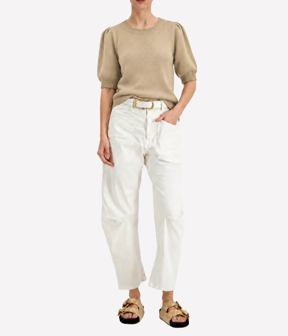 Model wearing the Avant Toi Cashmere Short Sleeve in Burro tucked into cream barrel-leg trousers with one hand in her pocket and dark sandals