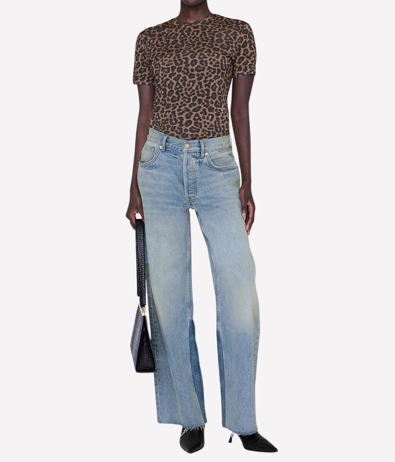 A model wearing a brown leopard-print short-sleeve top and light-wash wide-leg blue jeans, holding a black handbag against a plain light gray background.