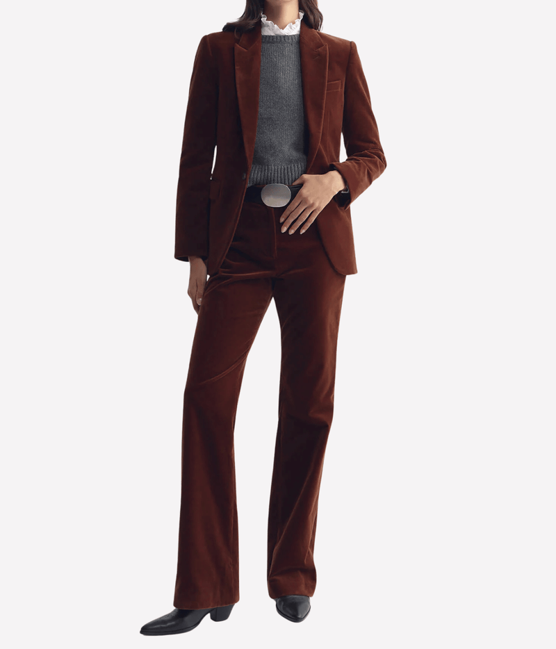 Full-length front view of a model wearing the Nili Lotan Anabel Tailored Jacket in Burnt Sienna open over a charcoal knit with matching flared trousers, a silver belt buckle and black pointed ankle boots