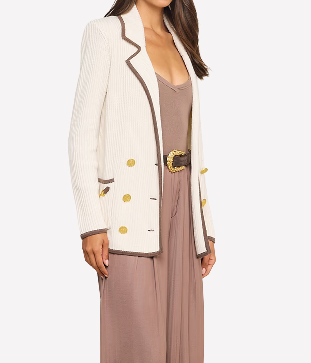 A woman wearing a cream knit blazer with brown trim and gold buttons.