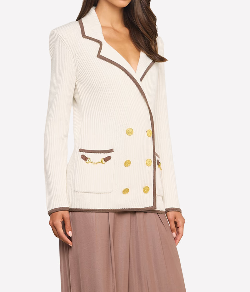 A woman wearing a cream ribbed knit blazer with brown trim and gold buttons, paired with taupe wide-leg pants, angled view