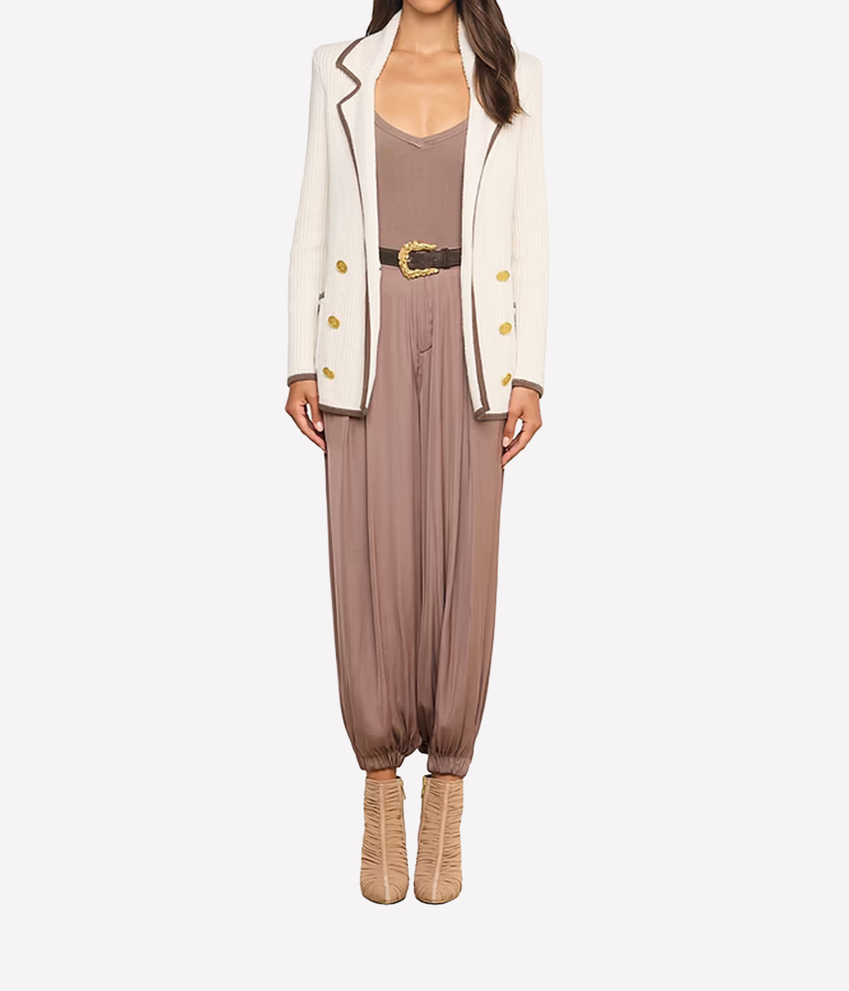 A woman wearing tan heeled boots, a taupe jumpsuit with a wide belt, and the Ranch Knit Blazer, a double-breasted white blazer with gold buttons.