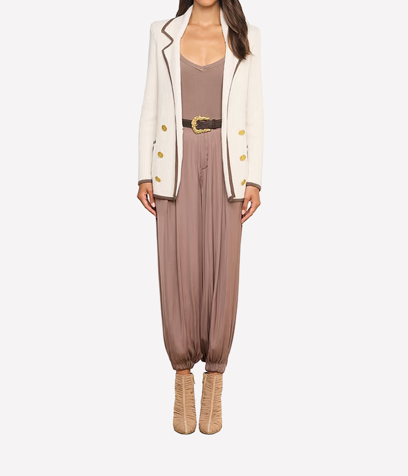 A woman wearing tan heeled boots, a taupe jumpsuit with a wide belt, and the Ranch Knit Blazer, a double-breasted white blazer with gold buttons.