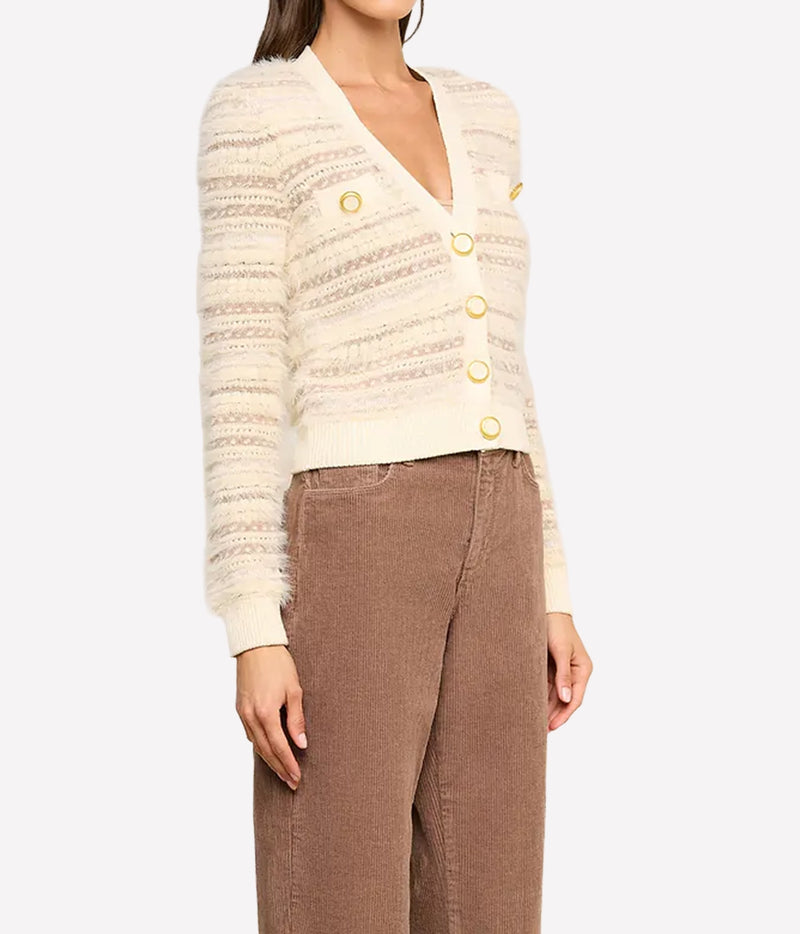 A model wearing a cream-coloured textured knit cardigan with gold buttons and brown corduroy trousers, angled view.
