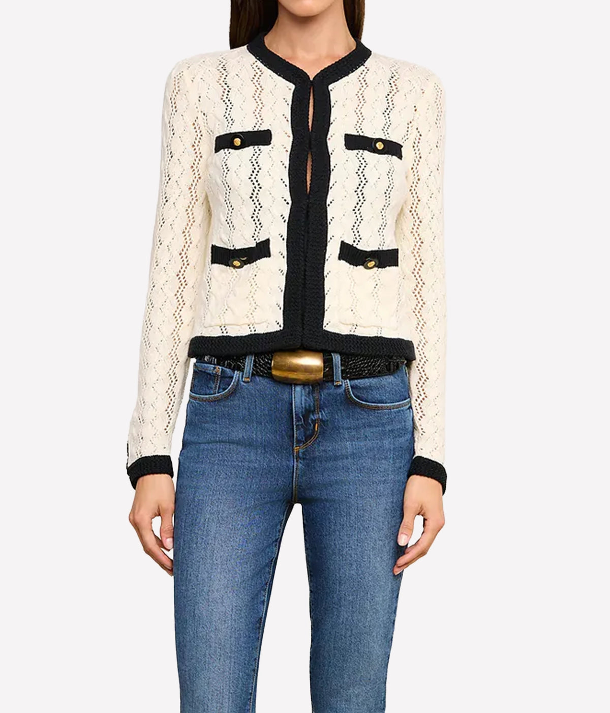 A woman wearing the L'AGENCE Zephyra Pointelle Knit Cardigan in Ivory & Black with black trim and gold-tone buttons, paired with blue jeans and a black belt with a gold buckle.