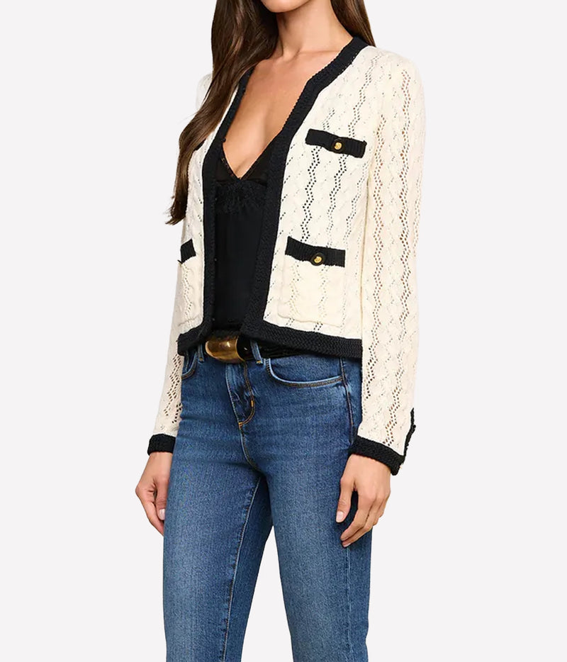 A woman wearing the L'AGENCE Zephyra Pointelle Knit Cardigan in Ivory & Black with gold-tone button accents, styled over a black top and blue jeans.