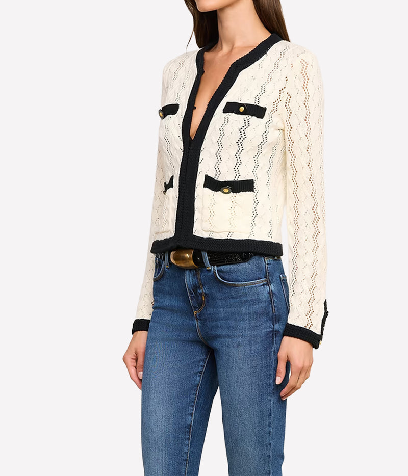 A woman wearing the L'AGENCE Zephyra Pointelle Knit Cardigan in Ivory & Black with black trim and gold-tone buttons, paired with blue jeans and a black belt.