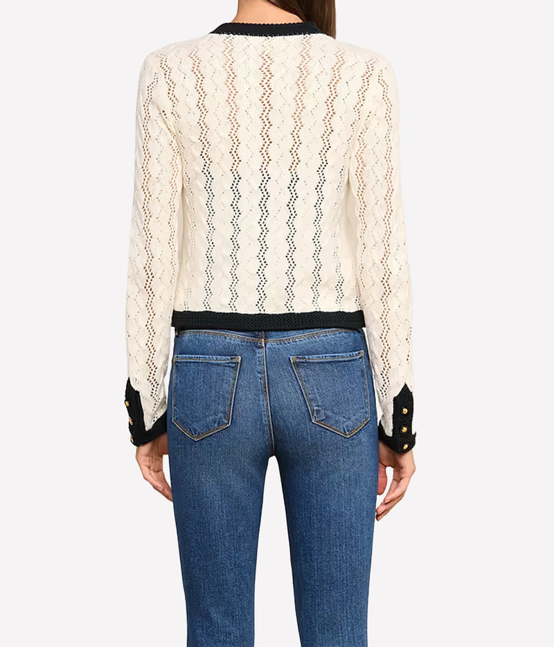 A woman viewed from the back wearing the L'AGENCE Zephyra Pointelle Knit Cardigan in Ivory & Black with black trim and blue jeans.