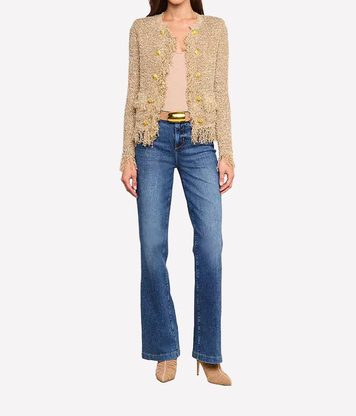 A woman wearing a natural coloured cardigan, a nude top, blue jeans, and beige heels stands facing forward.