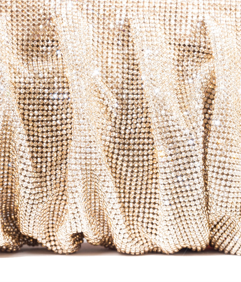 A close-up of a gold rhinestone-covered fabric with a shimmering, textured surface and soft folds.