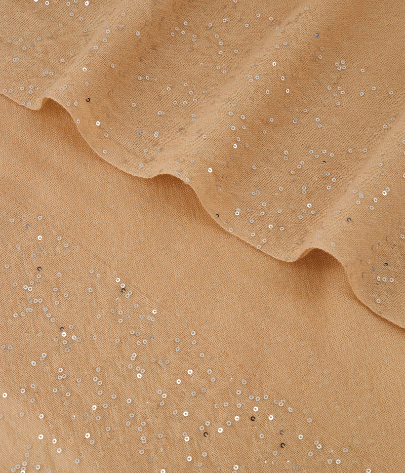 A close-up of beige fabric with scattered silver sequins and a ruffled edge
