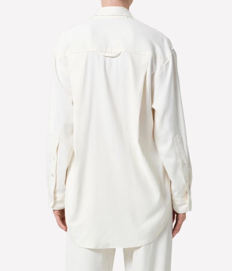 A person shown from the back wearing a long-sleeve cream-colored button-up shirt and matching light pants against a plain light gray studio background.