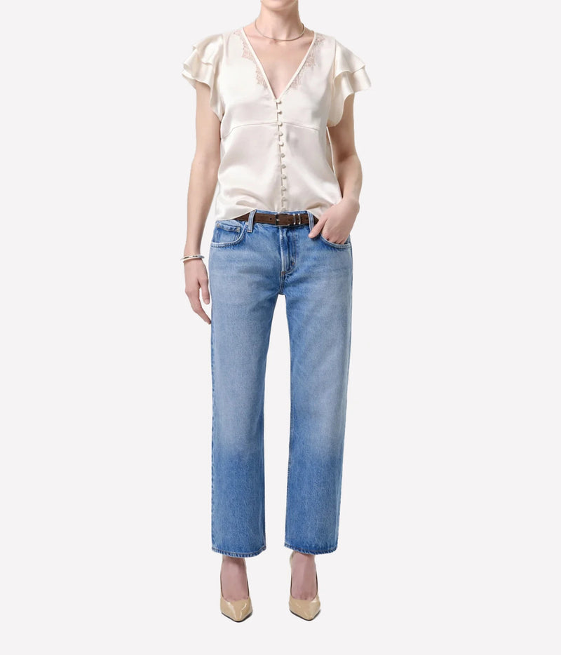 Full-length front view of a model wearing the Citizens Of Humanity Lola Flutter Lace Sleeve Top in Cream with mid-wash straight-leg jeans, a brown leather belt, gold choker necklace and nude heels