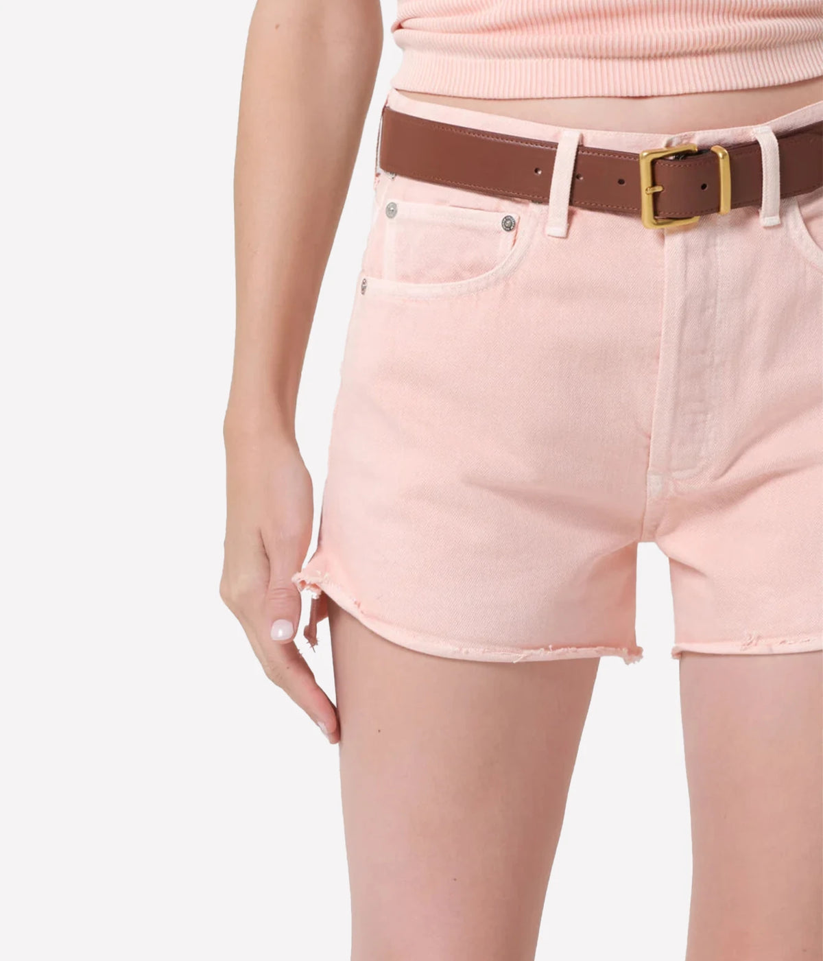 A close-up of a model wearing light pink denim shorts with a brown belt - Citizens of Humanity Marlow Denim Short in Pale Coral