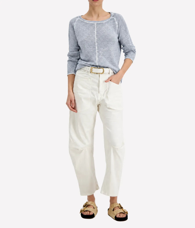 Model wearing the Avant Toi Maglia Pullover In Dusty Blue tucked into cream barrel-leg trousers with a brown leather belt and dark sandals
