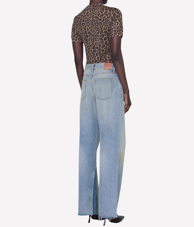 A model shown from the back wearing a leopard-print short-sleeve top and light-wash wide-leg denim jeans, paired with black pointed-toe heels, against a plain light gray background.