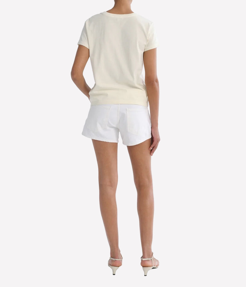 Back view of a model wearing the Agolde Low Rise Parker Short in Marshmallow with a cream tee and nude strappy heels, showing the back pockets and rear fit