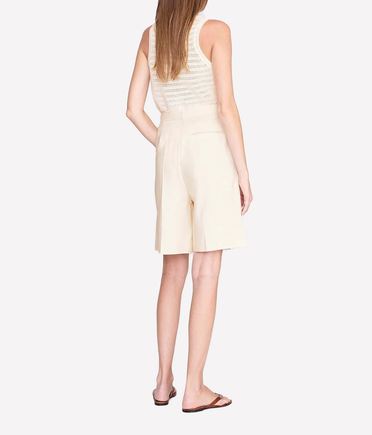 A woman shown from the back wearing a sleeveless cream-colored romper with a textured knit back panel and matching high-waisted shorts, paired with brown flat sandals against a light gray studio background.