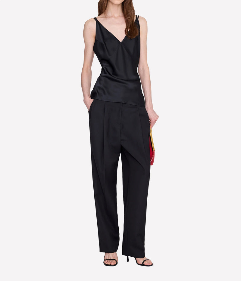 A model wearing a black satin camisole top and matching black wide-leg trousers, styled with black strappy heels and holding a small red and yellow clutch against a light gray background.