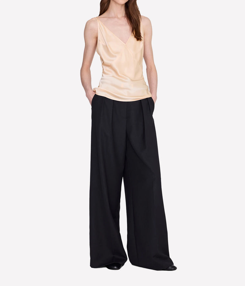 A model wearing a light beige satin camisole top and black wide-leg trousers, standing against a plain white studio background.