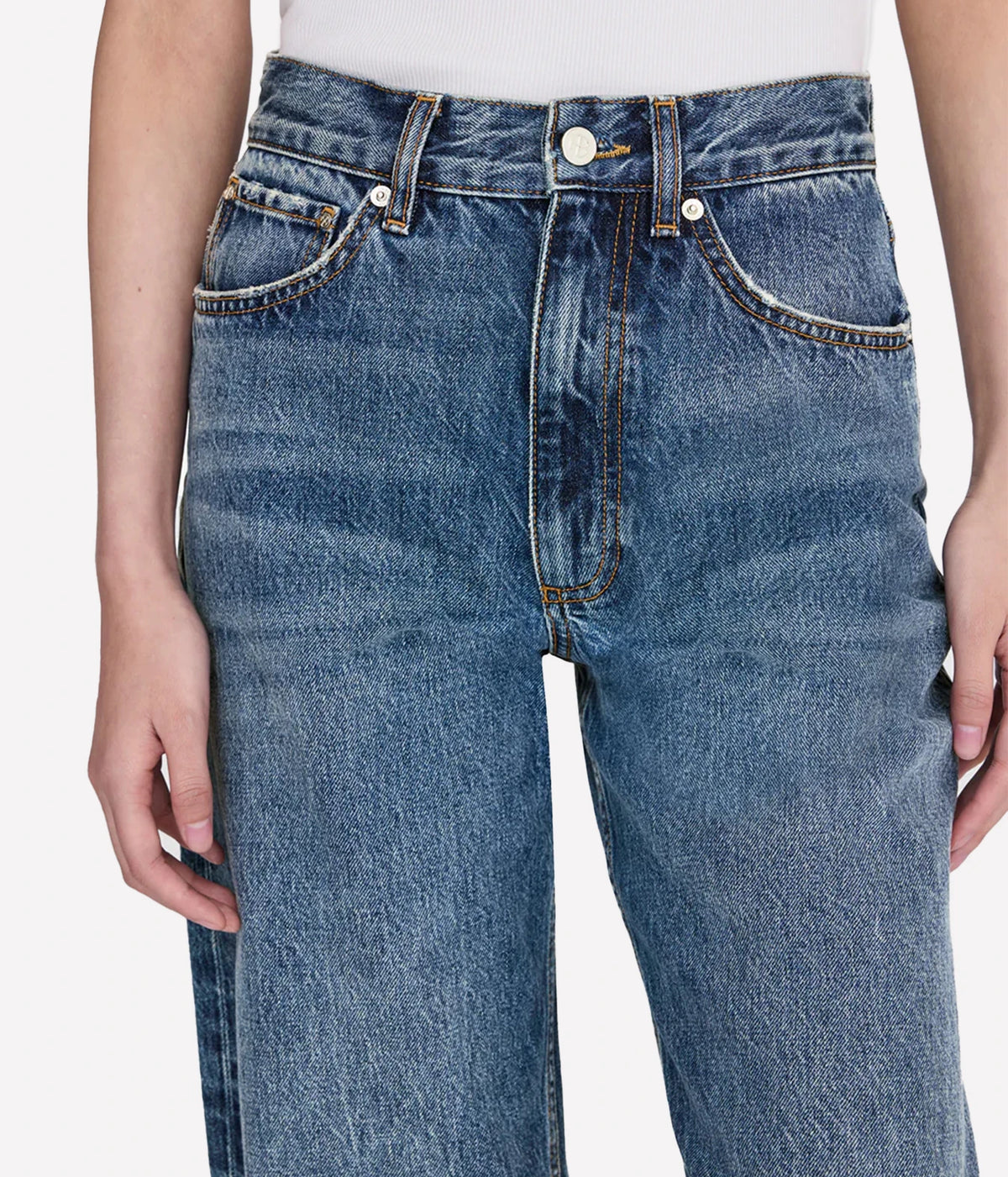 Close-up of a person wearing high-waisted blue denim jeans with a white top, shown from the waist to mid-thigh against a light gray studio background.