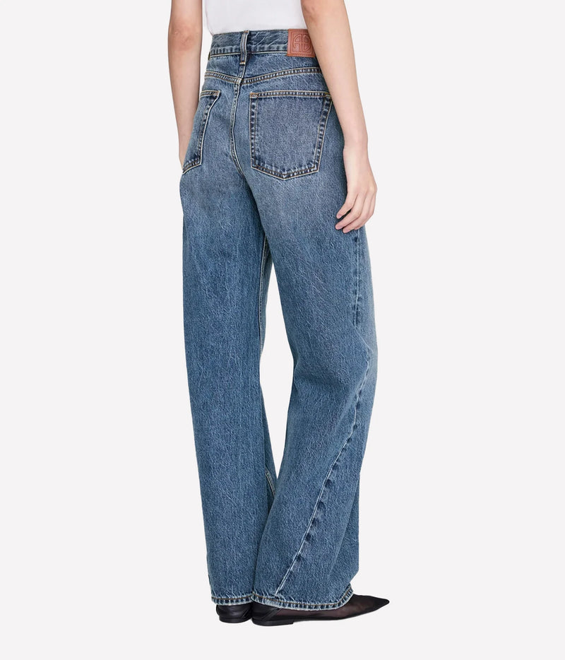 A person shown from the back wearing light-to-medium wash wide-leg jeans, a white top, and black pointed shoes against a clean light gray studio background.