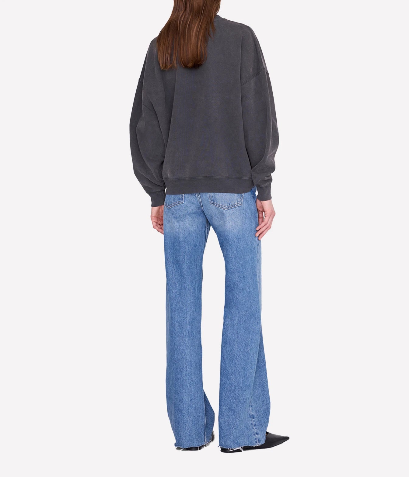 A model shown from the back wearing a dark charcoal gray oversized sweatshirt and light blue wide-leg jeans, set against a plain light gray background.