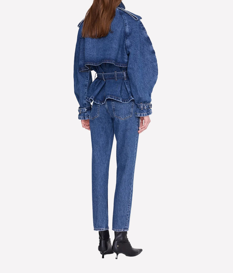 A model shown from the back wearing a blue denim set consisting of a cropped belted jacket with dramatic puffed sleeves and matching straight-leg jeans, paired with black ankle boots, on a light gray background.