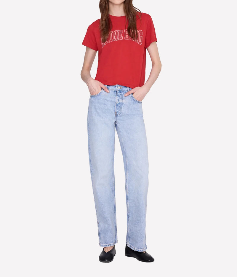 A model wearing a red graphic t-shirt and light-wash blue straight-leg jeans, standing against a light gray background.