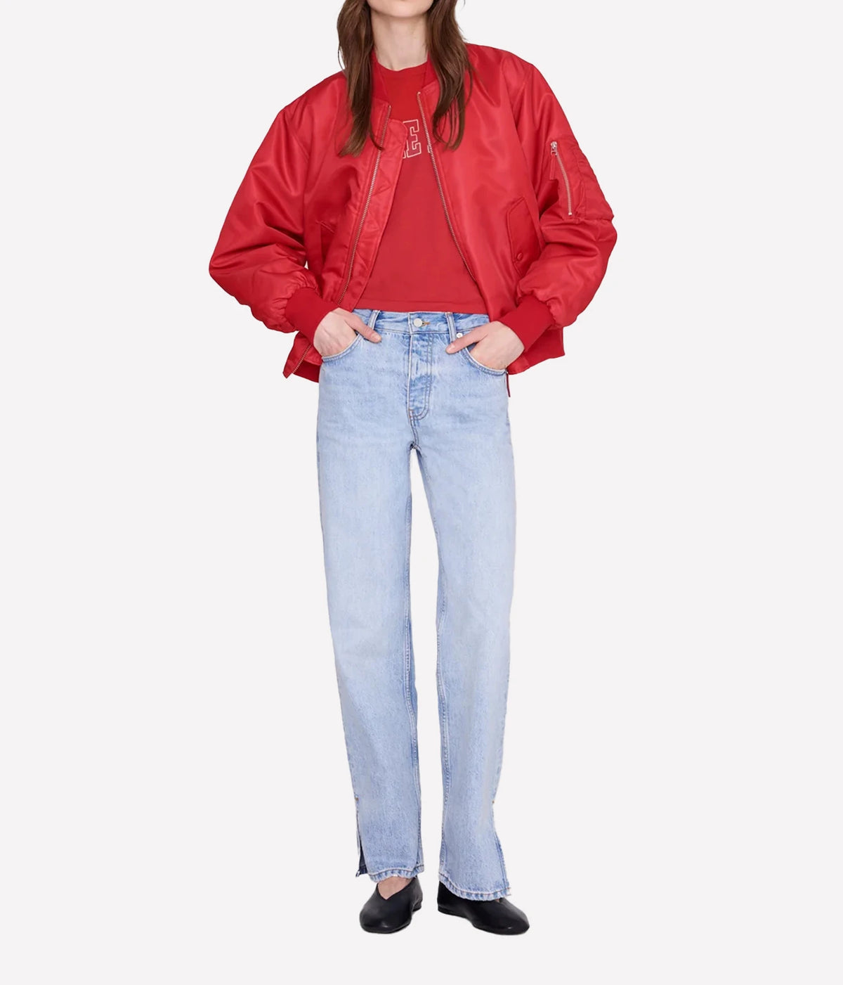 A model wearing a red satin bomber jacket over a matching red top, paired with light-wash blue jeans and black shoes, against a plain light gray background.