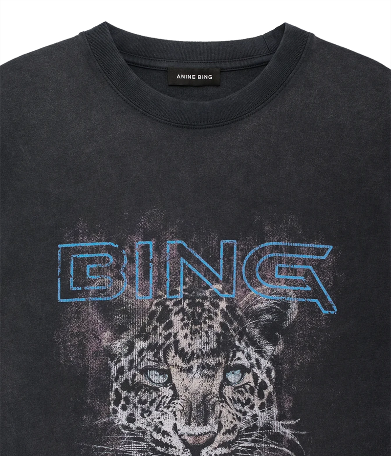 A close-up of a dark gray crewneck t-shirt featuring a distressed graphic of a leopard's face and the word 'BING' in blue outline lettering across the chest. The brand name 'ANNE BING' is visible on the inner neck label.