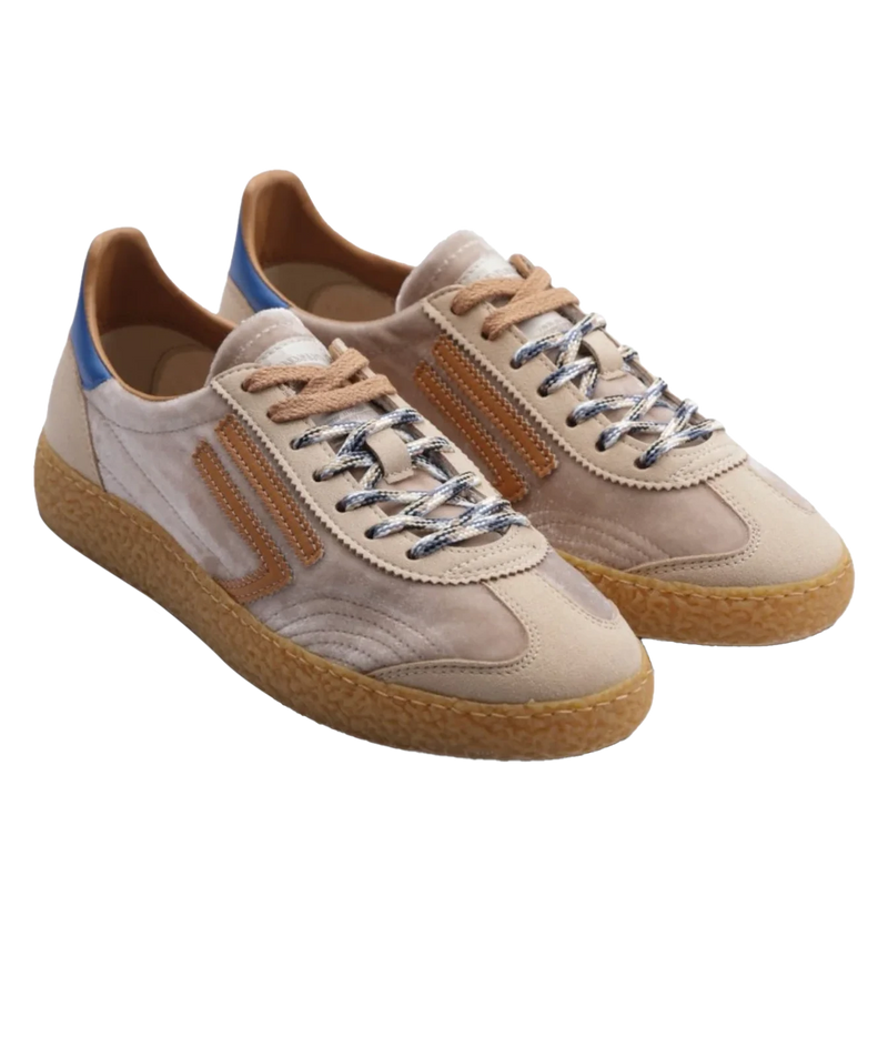 A pair of low-top suede sneakers in beige and light brown, featuring textured gum soles, metallic silver laces, and a small blue accent on the heel.