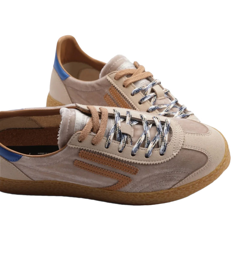 A pair of low-top sneakers in beige suede and leather, featuring metallic silver laces, a brown gum sole, and a small blue accent on the heel.