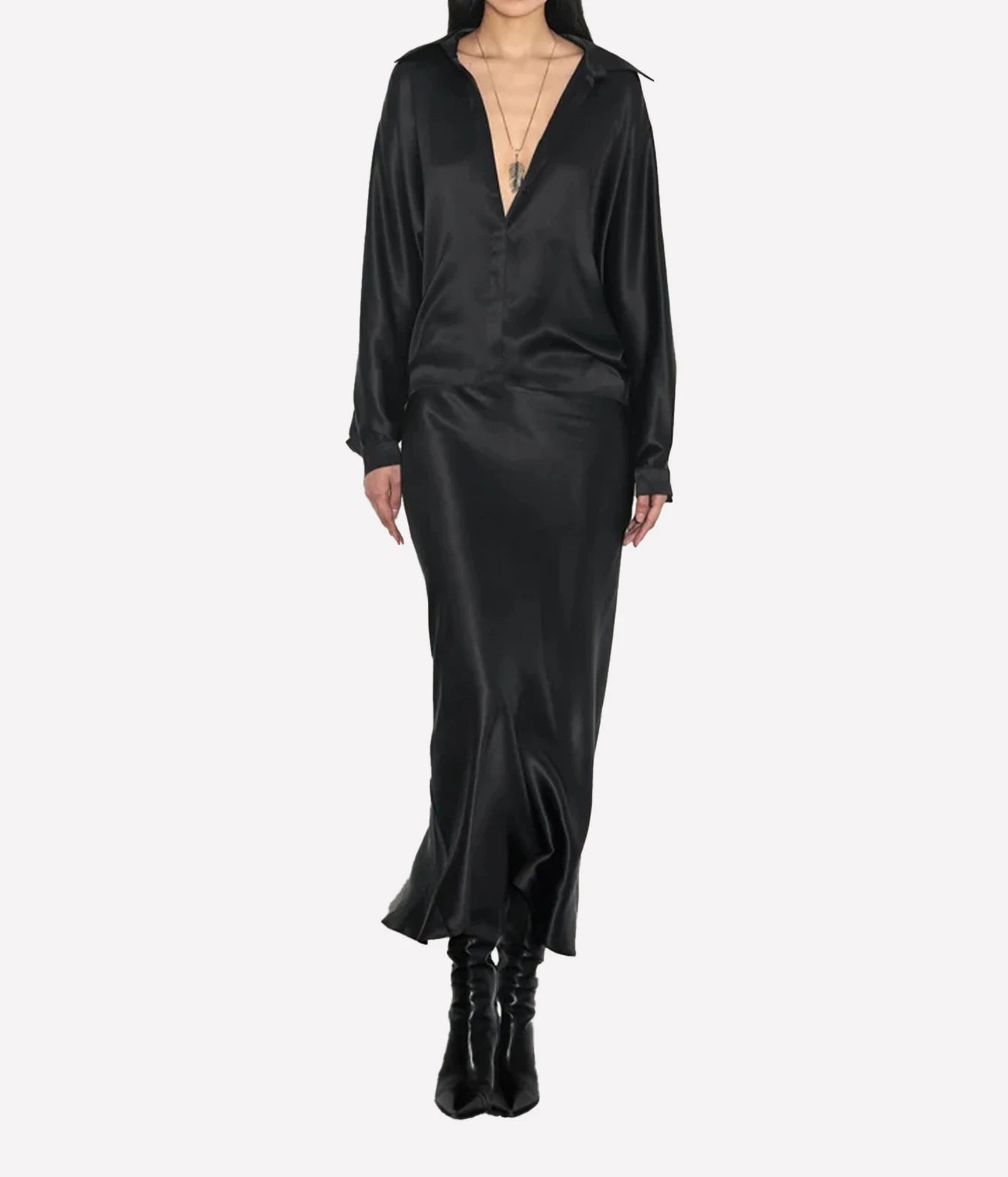 A model wearing a black satin long-sleeve midi dress with a deep V-neckline, paired with black leather ankle boots, shot against a solid light gray background.