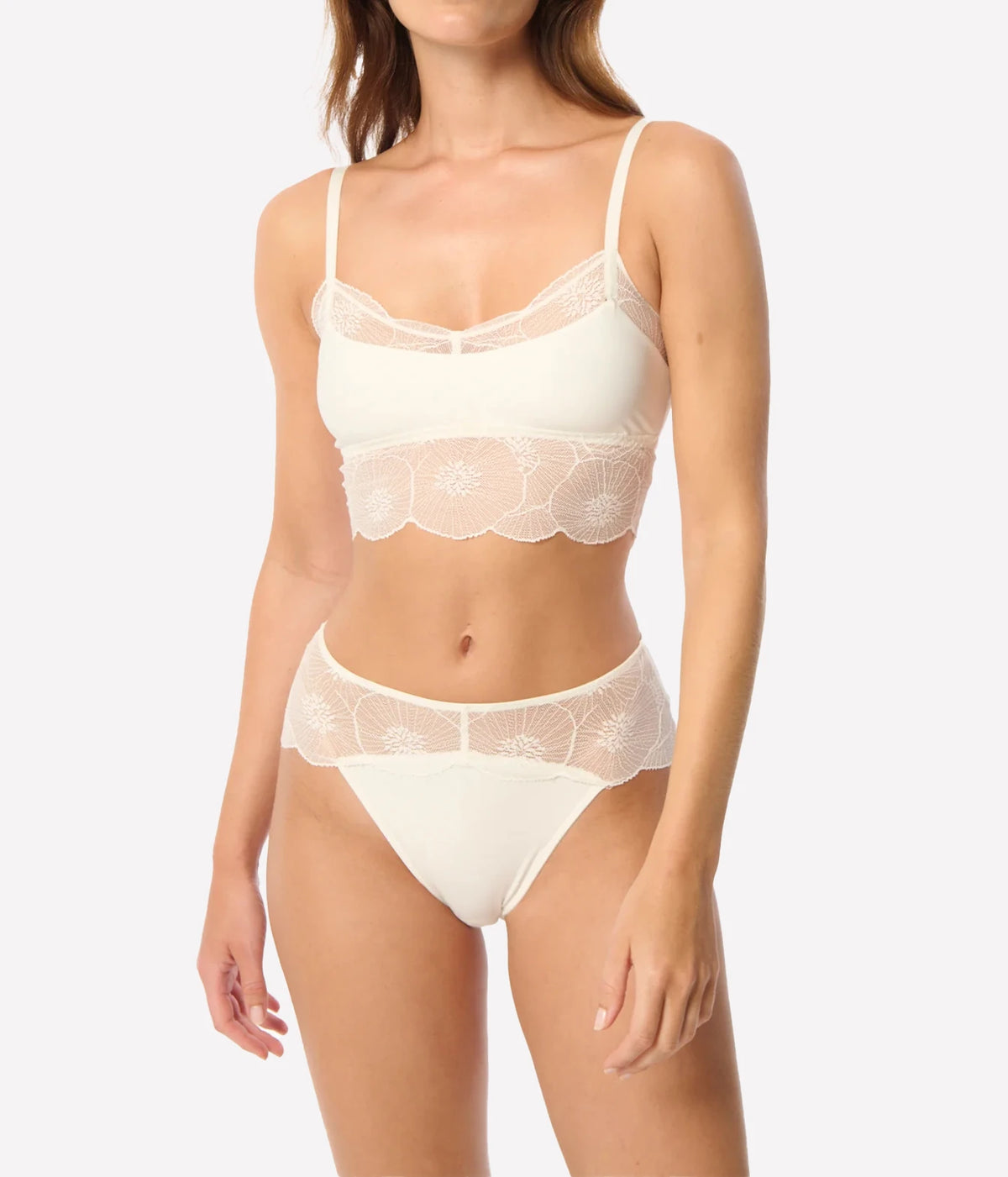 A model wearing a two-piece lingerie set in a warm off-white/cream color, featuring a bralette with floral lace trim and matching high-waisted briefs, Anemone Cropped Cami In Ivory