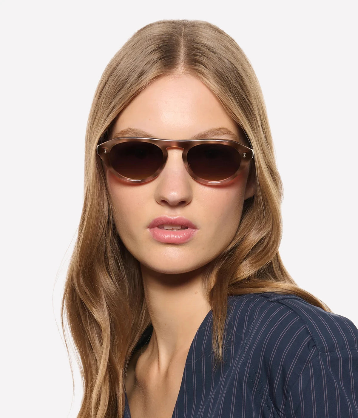 Model with long light brown hair wearing the KREWE Billie Sunglasses in Blush Tortoise with a navy top, front view