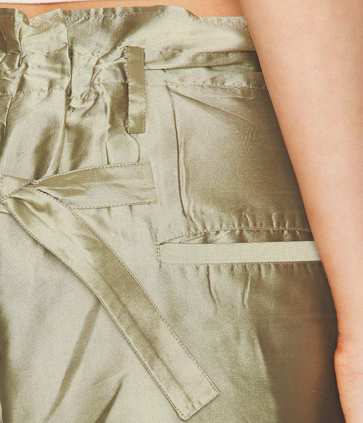 Close-up of sage green pants featuring an adjustable tie waist, belt loops and back welt pocket.
