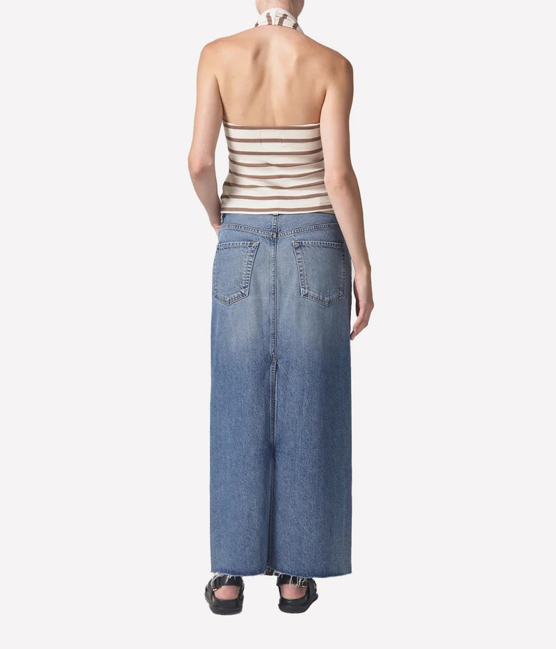 Full-length denim skirt with a raw hem and back slit detail, styled with a white tee and blazer for a modern, polished look.
