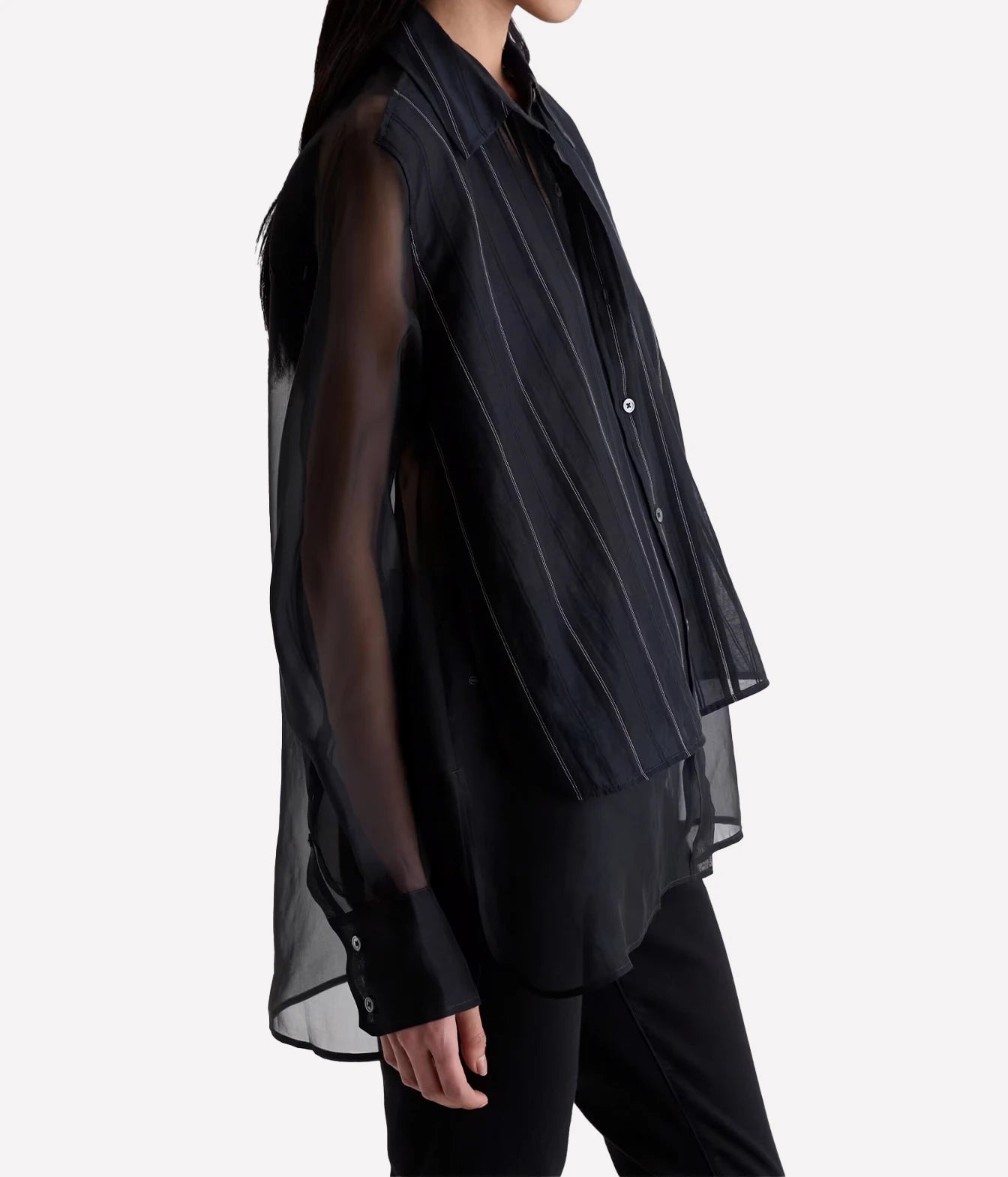 A side-profile view of a model wearing a black sheer mesh sleeveless vest over a black collared button-up shirt and black pants, set against a plain light gray background.