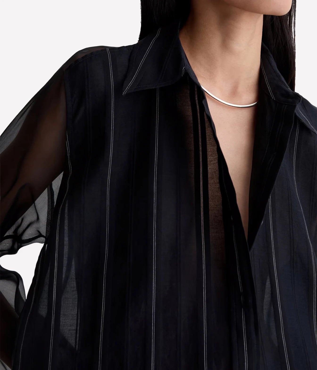 Close-up of a model wearing a sheer black button-up shirt with thin vertical white pinstripes and a silver curved necklace.