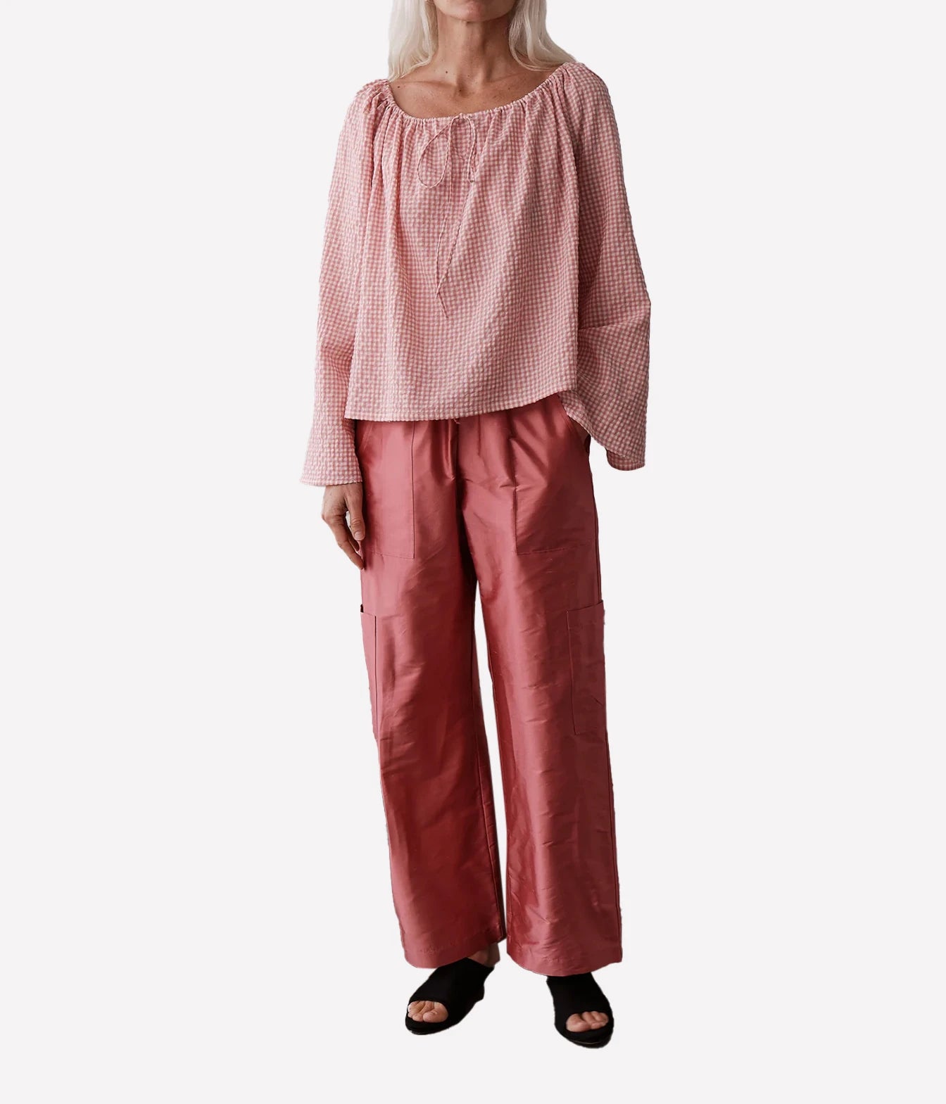 A model wearing a dusty pink gingham long-sleeve top and matching dusty rose wide-leg pants, paired with black slide sandals, against a plain white background.