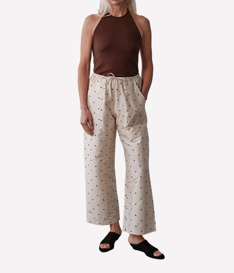 A model wearing a brown halter top and beige wide-leg drawstring pants with a small black polka dot pattern, paired with black slide sandals, against a plain light gray background.